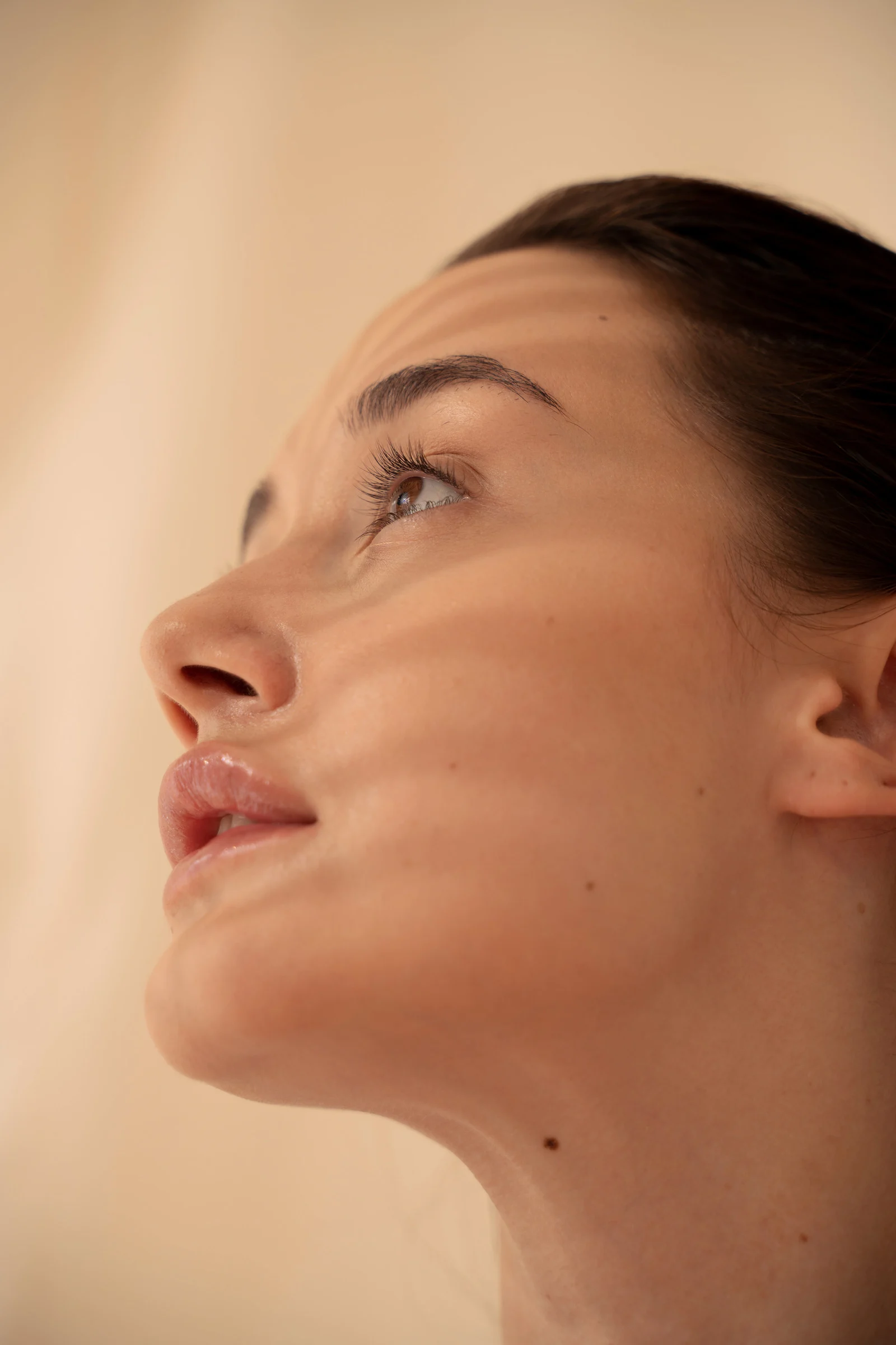 Close-up of a woman with under-eye gel patches, natural makeup, and smooth skin, against a neutral beige background