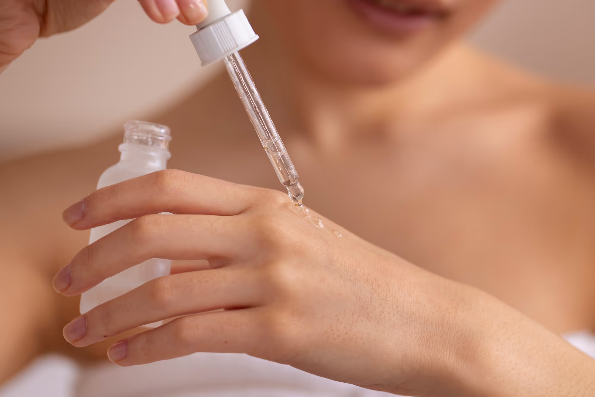 Close-up of a woman applying serum drops onto her hand using a dropper bottle